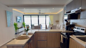 A modern kitchen with a central island, wooden cabinets, a built-in oven, and a large window providing natural light.