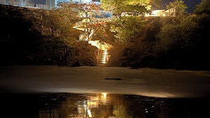 A nighttime view of a building with a red light on top, surrounded by trees and a body of water reflecting the lights.