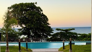 A pool area with a view of the sea, surrounded by greenery and a paved walkway.