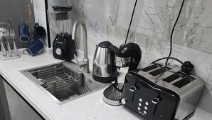 Une cuisine équipée d’une hotte en acier inoxydable, d’une machine à café, d’un grille-pain et d’une bouilloire posés sur le plan de travail.