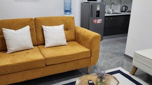 Un salon avec un canapé de couleur moutarde, une table basse avec une télécommande et un tableau représentant une girafe accroché au mur.