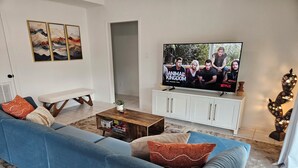 Una sala moderna con un sofá azul, una mesa de centro de madera y un televisor de pantalla plana mostrando un programa.