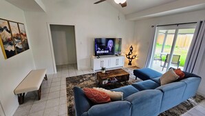 Una sala de estar con sofá azul, una mesa de centro, televisor y ventilador de techo.
