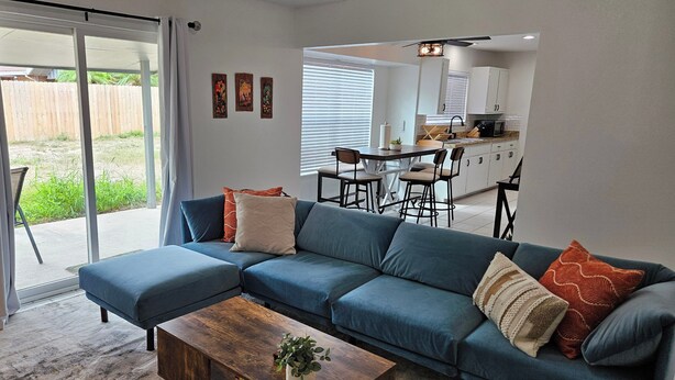 Una sala de estar con un sofá seccional azul, una mesa de centro de madera y un ventanal corredizo que da a un patio.
