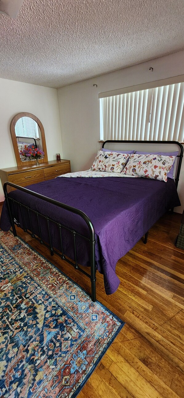 A bedroom with a bed, a wooden dresser, a mirror, and a patterned rug.