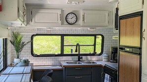 A compact kitchen with a window, a clock, and a stove. - Waterfront RV Escape in Amish Country (Glenmont)