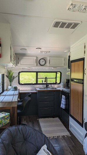 A compact kitchen with a window, a clock, and a stove.