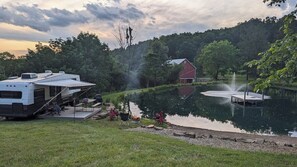 A lakeside RV campsite with a dock, a red barn, and a fountain.