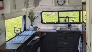A compact kitchen with a window view, a sink, cabinets, and a clock. - Waterfront RV Escape in Amish Country (Glenmont)