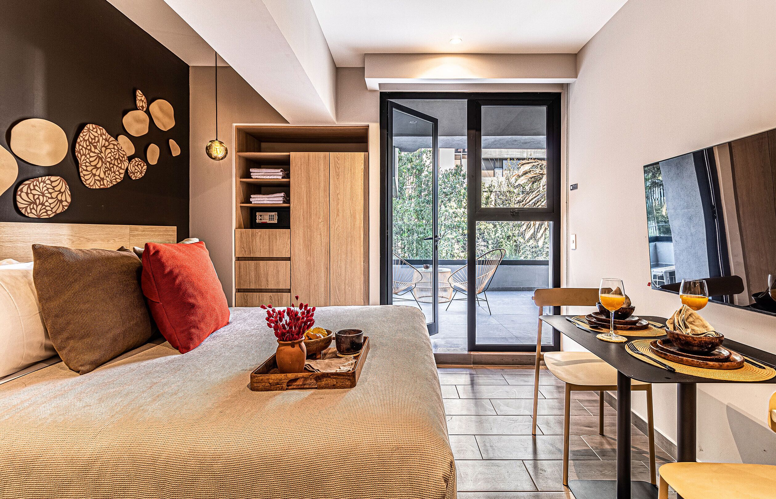 Un dormitorio moderno con una cama grande, un comedor con desayuno preparado y vistas al exterior por una puerta corredera.