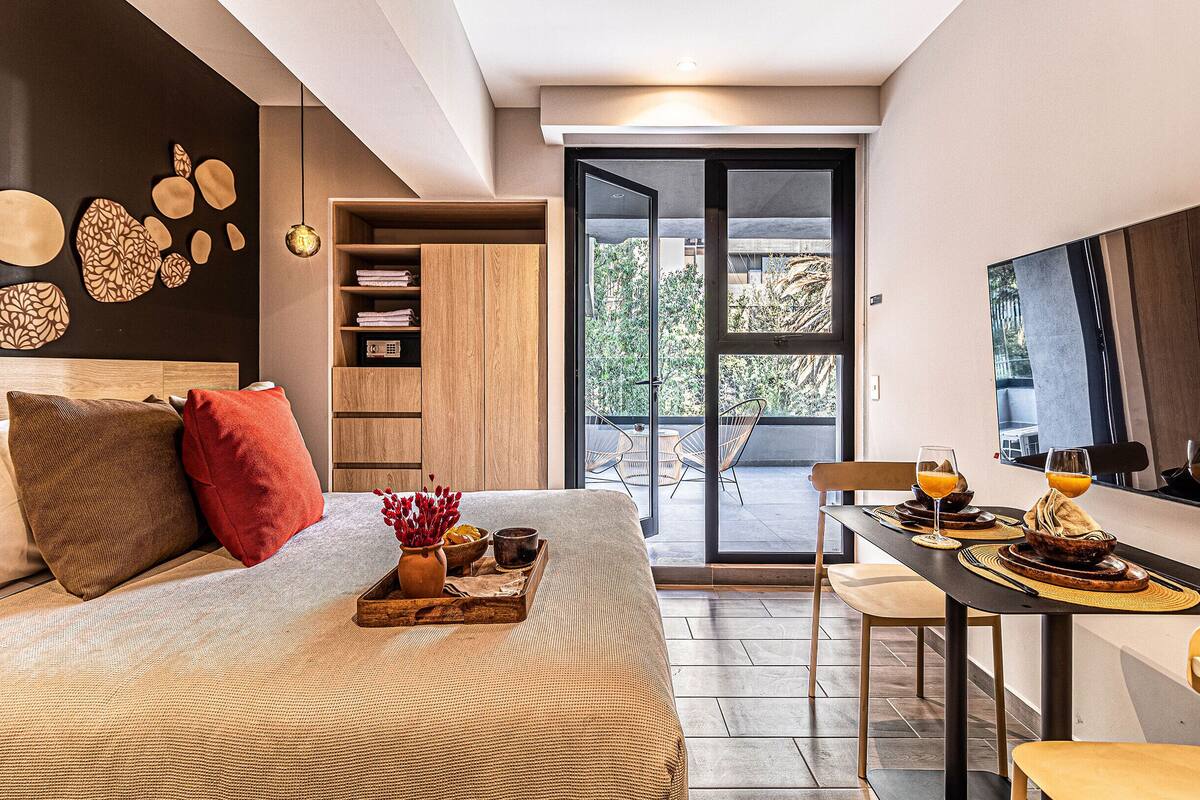 Une chambre moderne avec un grand lit, un coin repas avec une table préparée pour le petit-déjeuner, et une vue sur l’extérieur grâce à une porte coulissante.