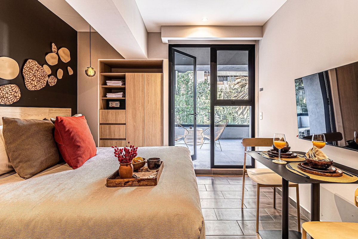 Un dormitorio moderno con una cama grande, un comedor con desayuno preparado y vistas al exterior por una puerta corredera.
