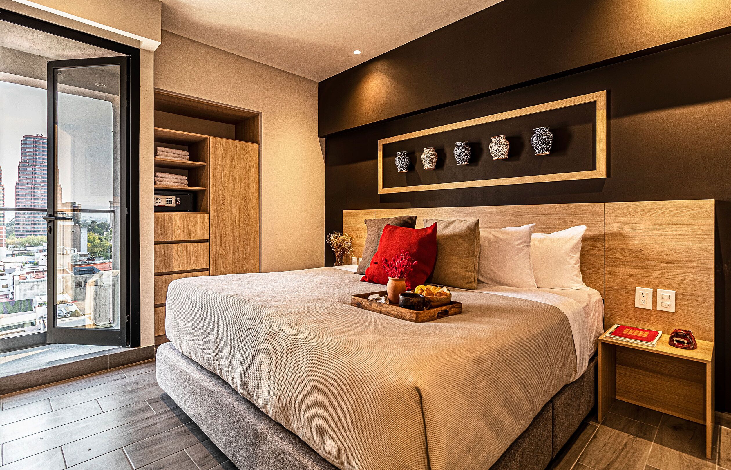 Un dormitorio moderno con una cama grande, cabecera de madera y vista a la ciudad a través de una puerta corrediza.