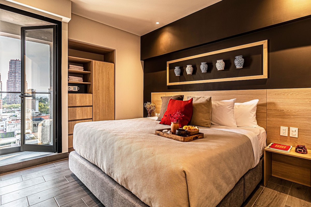 Un dormitorio moderno con una cama grande, cabecera de madera y vista a la ciudad a través de una puerta corrediza.
