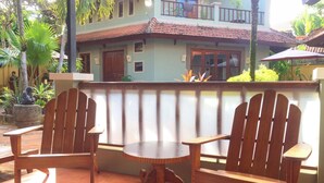 Un edificio de dos pisos con balcón, sillas de madera y una pequeña mesa.