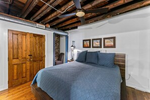Una camera da letto con soffitto in legno, un letto con copriletto blu, una porta in legno e un muro in mattoni.