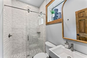 Un bagno moderno con cabina doccia in vetro, un water bianco, un lavabo con piano in legno e uno specchio con cornice in legno.