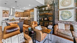 A modern kitchen with stainless steel appliances, a dining area with leather sofas, and a living room with a brick wall and artwork.