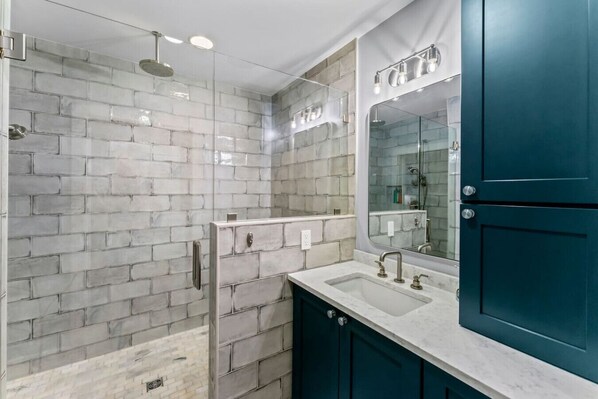 Une salle de bain moderne avec une douche à l’italienne en verre, un grand miroir et des meubles de couleur turquoise.