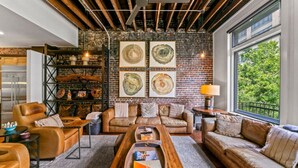 A cozy living room with leather sofas, a wooden coffee table, and a brick wall with artwork.