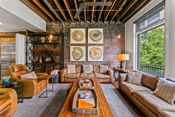 A cozy living room with leather sofas, a wooden coffee table, and a brick wall with artwork. - Amazing Rooftop Patio Overlooking Gay street (Knoxville)