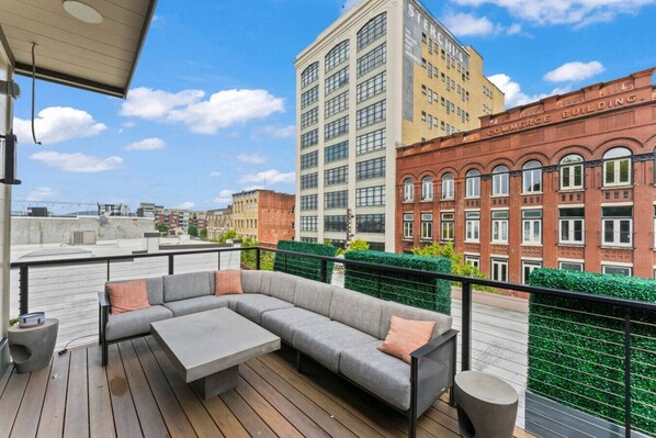 Una terrazza sul tetto con un divano angolare grigio, un tavolino e uno sgabello rotondo. La terrazza si affaccia su un panorama urbano con un mix di edifici moderni e storici.