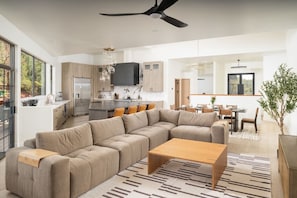 A modern living room with a sectional sofa, a wooden coffee table, and a dining area with a table and chairs. - Cathedral Shadows with Heated Pool & Spa, Sauna, Firepit, Gym (Sedona)