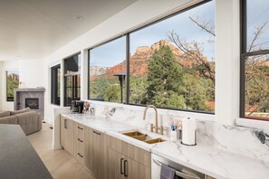 A modern kitchen with large windows, a fireplace, and a view of red rock formations. - Cathedral Shadows with Heated Pool & Spa, Sauna, Firepit, Gym (Sedona)