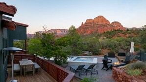Una terrazza con arredi da esterno, un braciere e una vasca idromassaggio, immersa nel verde e con vista su formazioni rocciose rosse.
