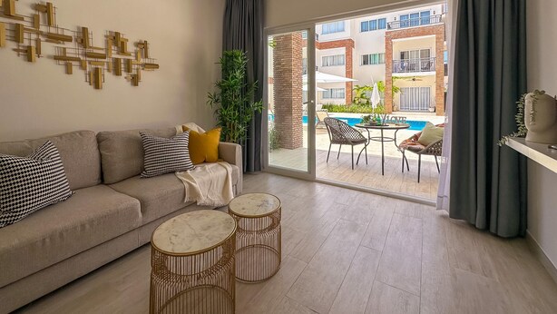 A modern living room with a sofa, two round side tables, a large window with a view of a pool and buildings.
