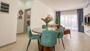 A modern dining area with a round glass table, teal upholstered chairs, and a vase with flowers.