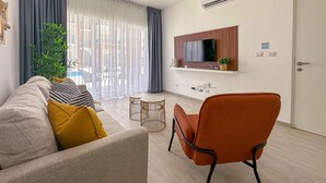 A modern living room with a sofa, a coffee table, and a chair. There is a TV mounted on the wall and an air conditioning unit above it.