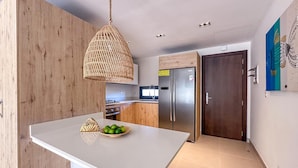 A modern kitchen with a large island, a stainless steel refrigerator, and a hanging light fixture.
