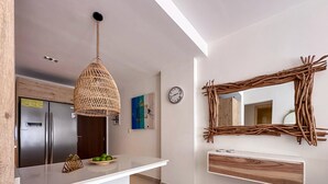 A modern kitchen with a white countertop, a hanging woven light fixture, a wooden-framed mirror, and a clock on the wall.