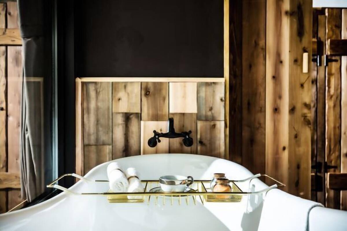 A modern bathroom with a white bathtub, wooden panel wall, and a gold tray with toiletries.