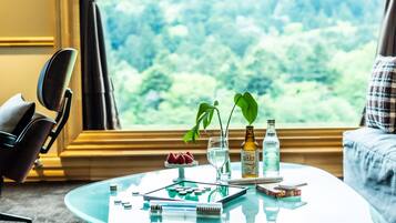 Habitación con una mesa de vidrio, una silla, un sofá y una ventana que da a zonas verdes.