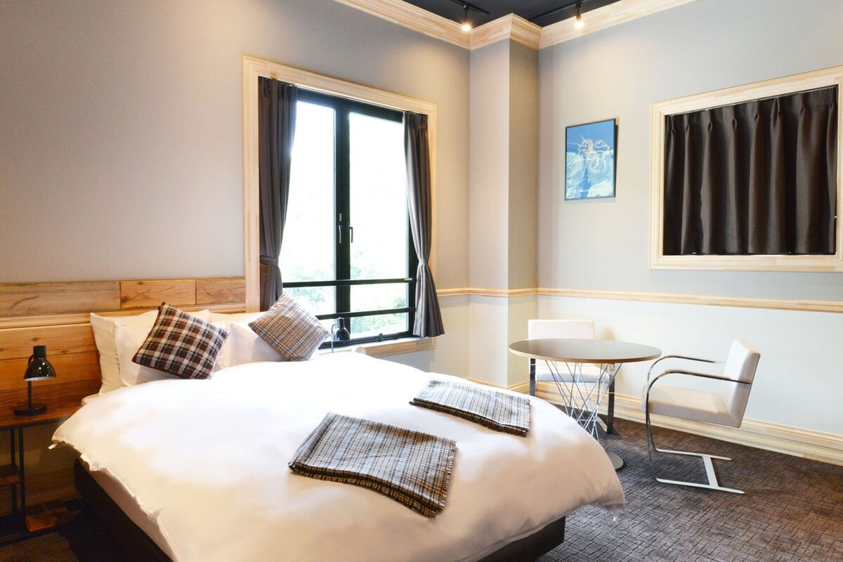 A hotel room with a large bed, a desk, a chair, and a small table.