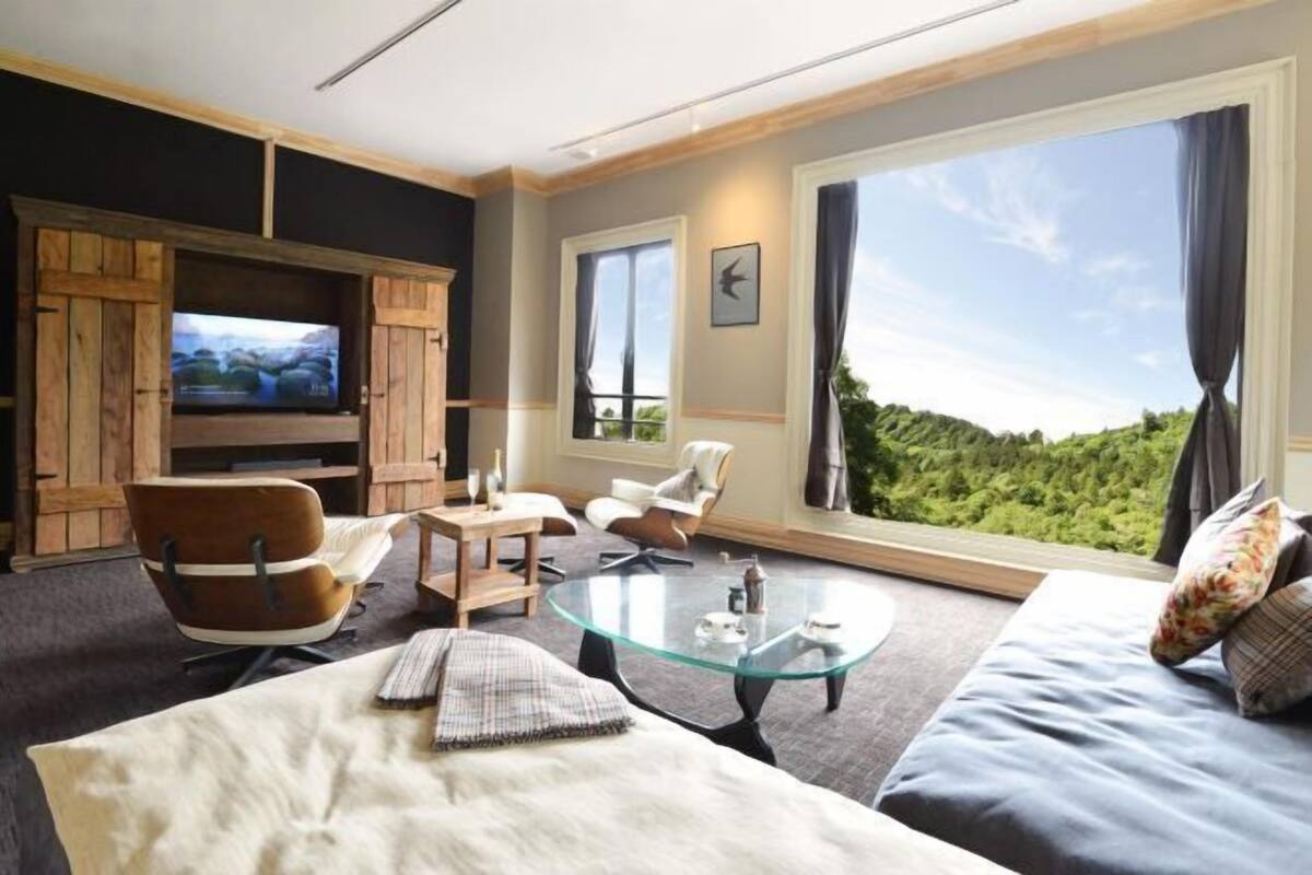 A modern living room with a large TV, comfortable seating, a glass coffee table, and a scenic view.