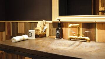 Una encimera de madera con una botella de desinfectante de manos, una toalla enrollada y un neceser de madera.
