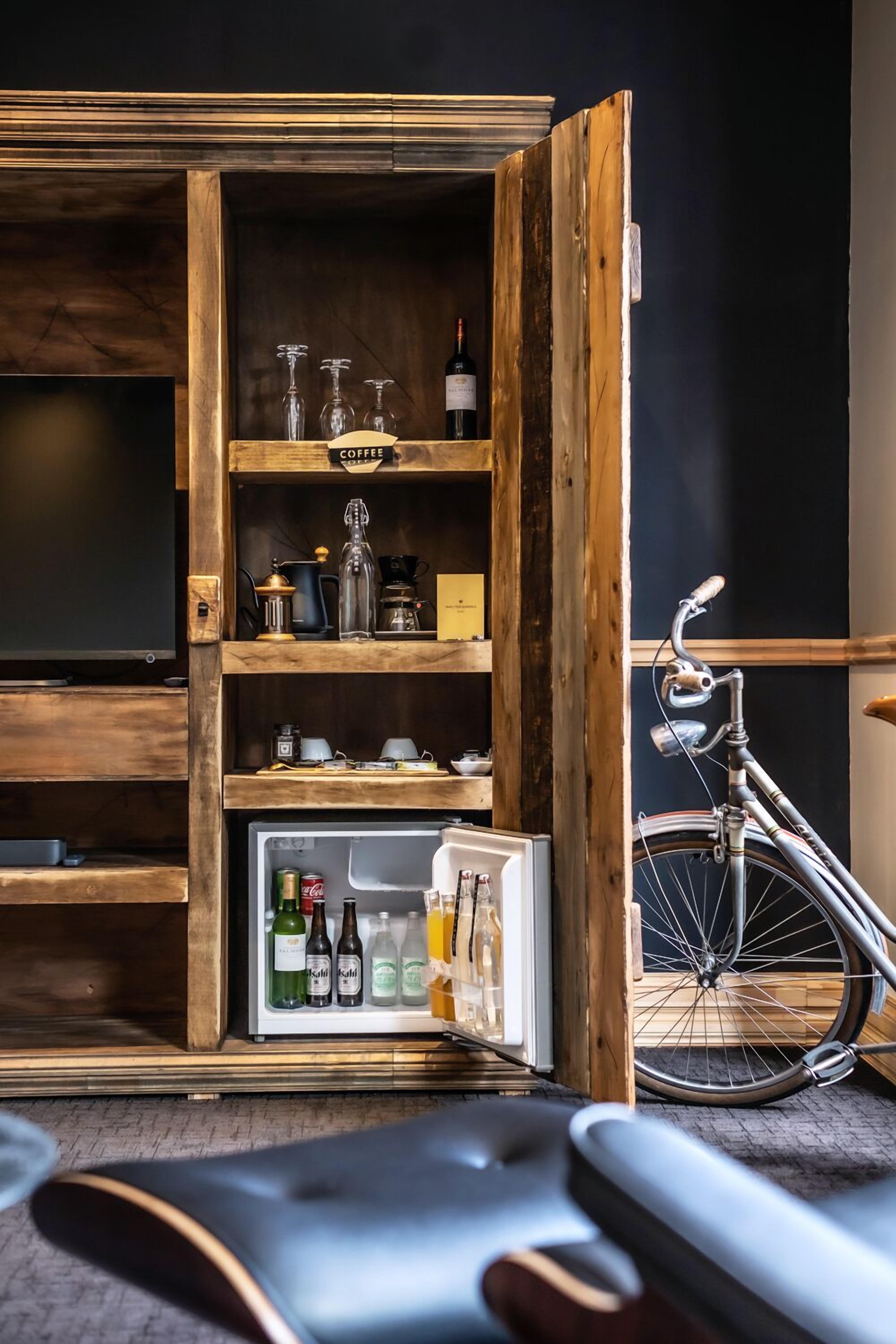 Habitación compacta con un mueble de madera que contiene un refrigerador lleno de bebidas, una bicicleta y diversos utensilios de cocina.