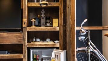 Habitación compacta con un mueble de madera que contiene un refrigerador lleno de bebidas, una bicicleta y diversos utensilios de cocina.