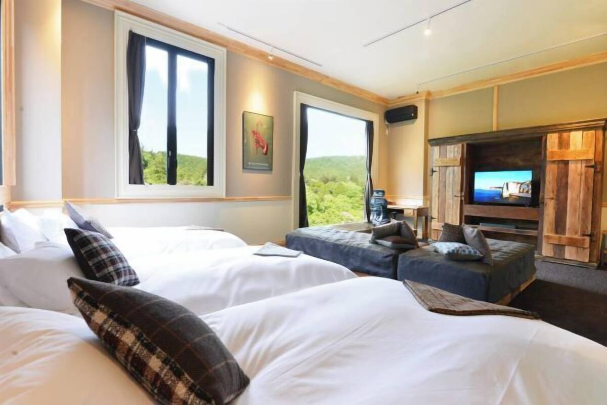 A hotel room with two beds, a television, and a large window with a view of greenery.