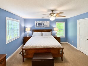 A bedroom with a bed, two bedside lamps, a ceiling fan, and a window with blinds.