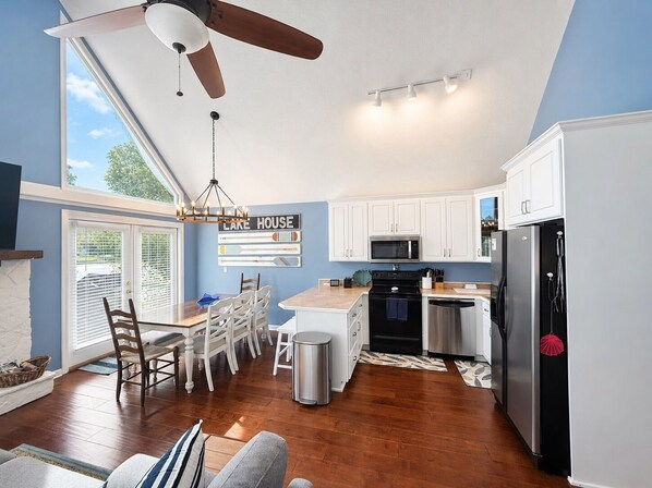A modern kitchen with white cabinets, a stainless steel refrigerator, and a dining area with a table and chairs. - Lake Sinclair Escape - boathouse, 4 bedroom (Sparta)