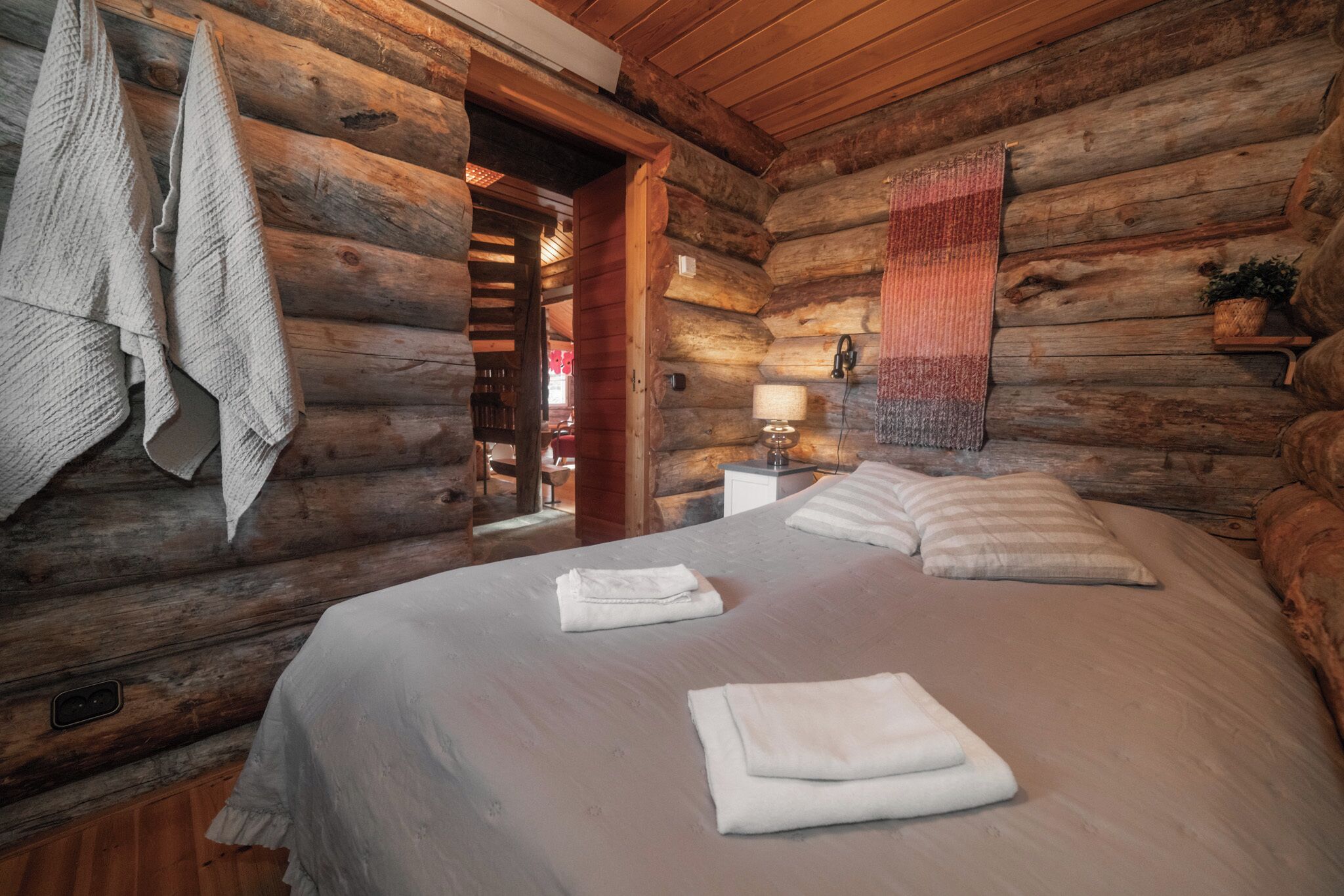 A log cabin room with a bed, towels, a lamp, and a plant.