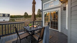 A deck with a table and chairs, a patio umbrella, and a view of a house and trees.