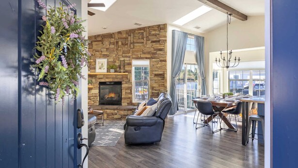 A modern living room with a stone fireplace, a dining area with a chandelier, and a view of the outdoors.