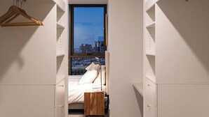 A bedroom with a city view, a bed, a bedside table, and a wardrobe.