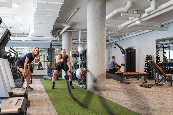 Un gimnasio con equipamiento de ejercicio, una cinta de correr y una zona con colchonetas verdes.