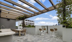 Une terrasse extérieure avec un sol en pierre, une table entourée de chaises et une structure en forme de pergola.